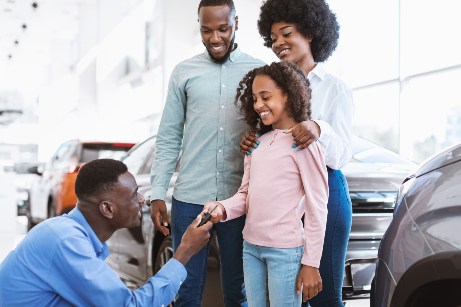 Happy black family buying new car, salesman giving them key at auto dealership. Afro clients making deal with manager, purchasing modern vehicle at automobile showroom